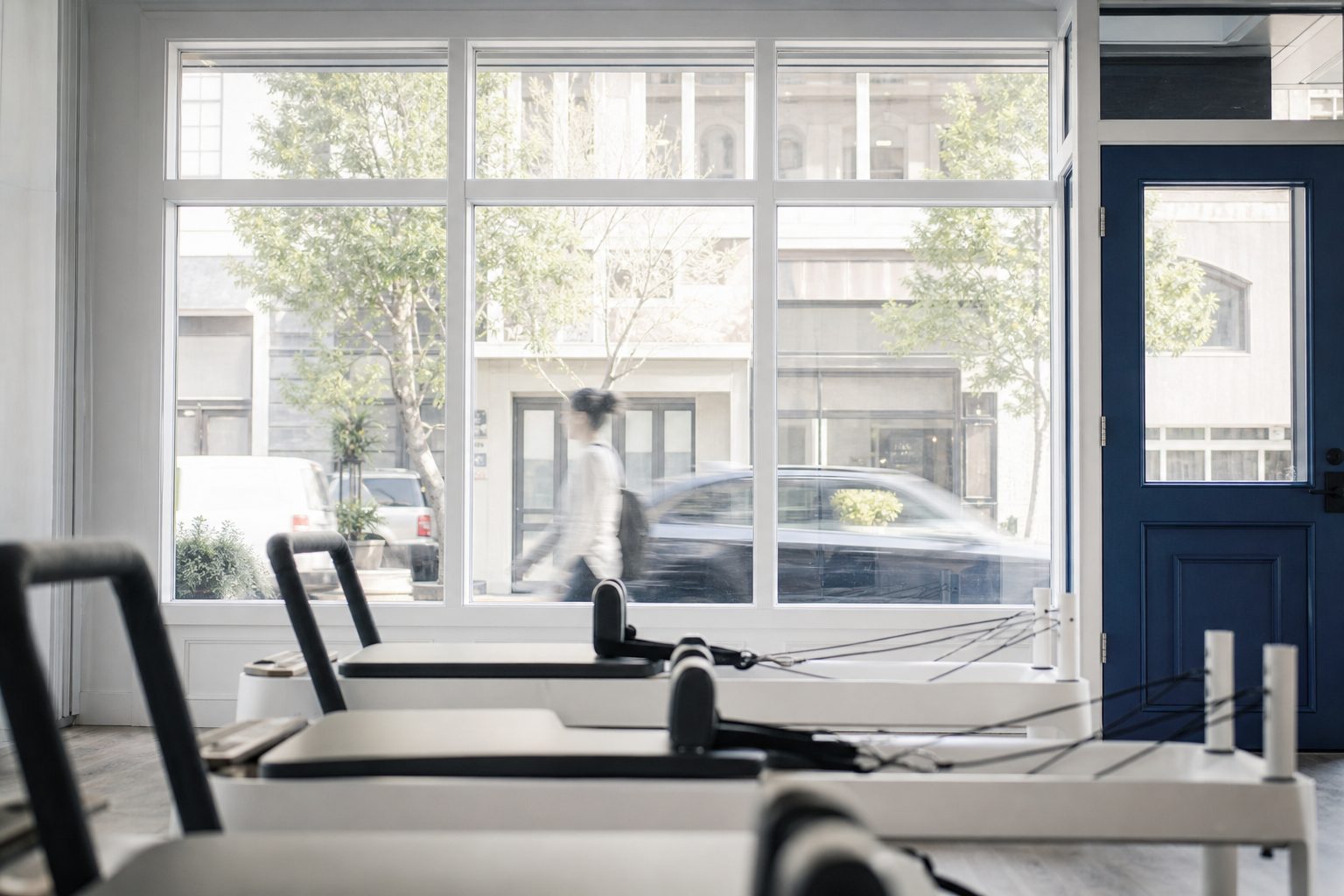 View from inside a bright Pilates studio toward the storefront window with reformers in soft focus
